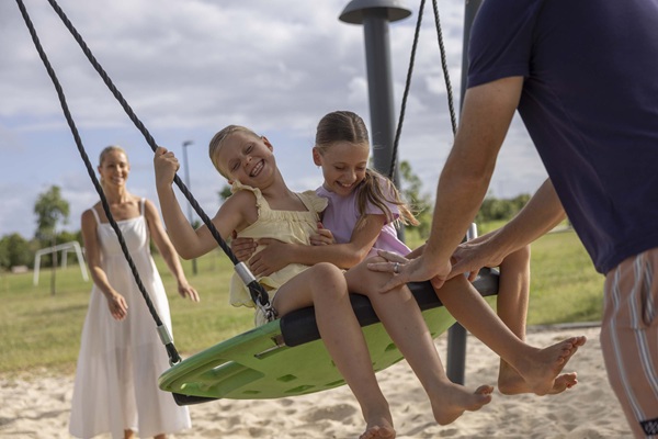 Two girls laughing on playground swing with parents